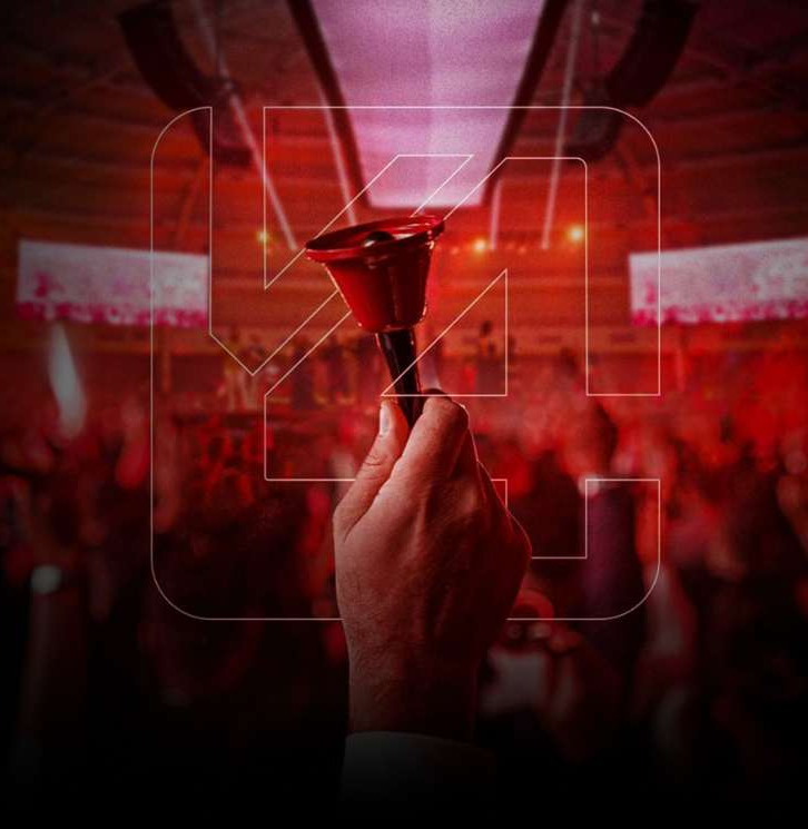Mão segurando um sino vermelho em um evento, com o logo V4 em destaque